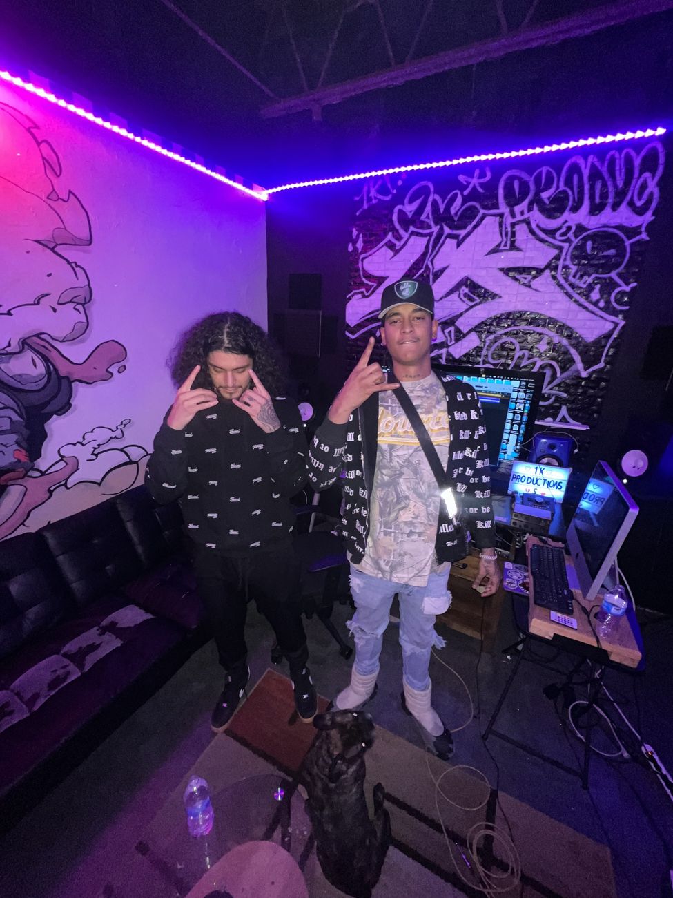 Two artists posing in front of a graffiti wall and studio setup